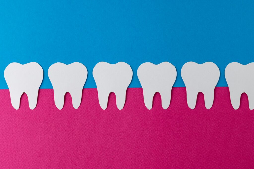 Row of white teeth set in pink gums on blue background, symbolizing the importance of gum health for a healthy smile, for Wells Family Dental's blog on gum health's impact