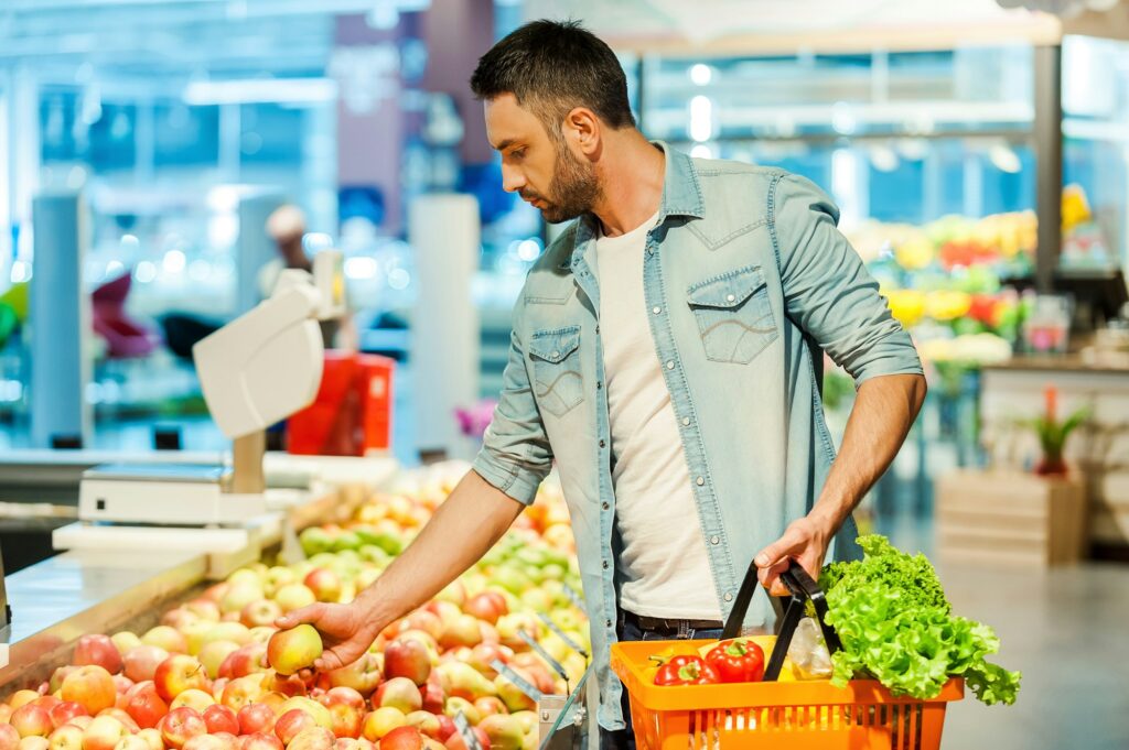 Man selecting fresh produce in grocery store, highlighting the link between nutrition and dental health, for Wells Family Dental's blog on diet's impact on oral health