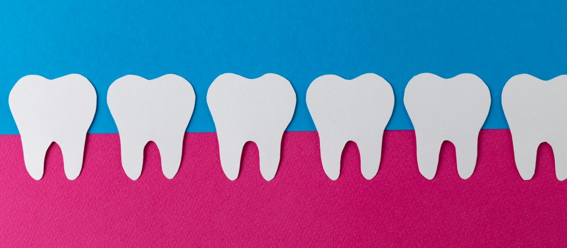 Row of white teeth set in pink gums on blue background, symbolizing the importance of gum health for a healthy smile, for Wells Family Dental's blog on gum health's impact