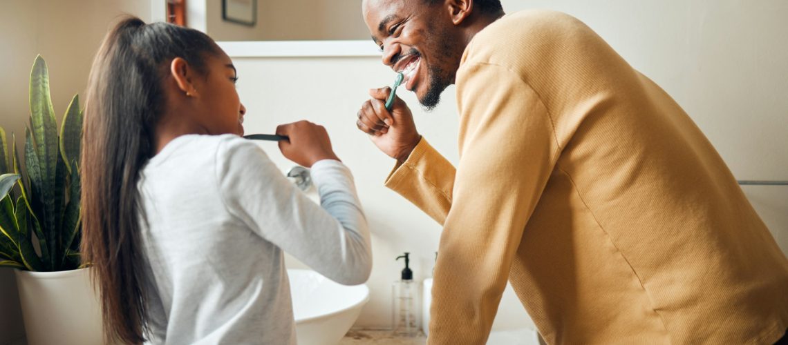 Father and daughter brushing teeth together in bathroom mirror, promoting family dental care and healthy habits.