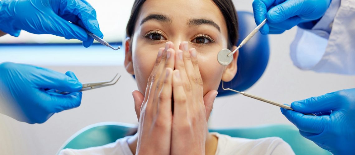 "Woman showing dental anxiety with dentists and tools nearby, illustrating fear of dental visits for Wells Family Dental's blog on overcoming dental anxiety